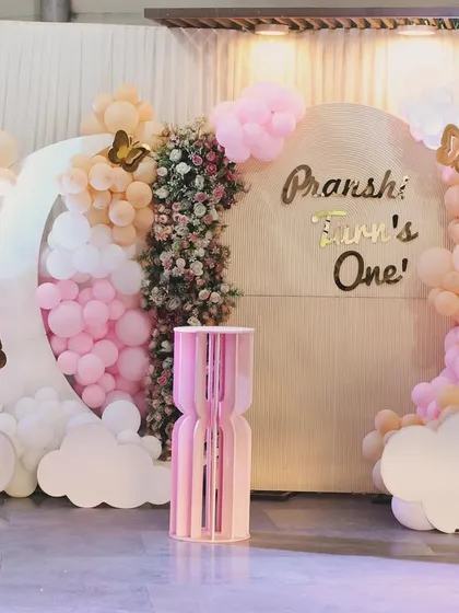 A dreamy and whimsical first birthday for Pranshi. The decor features a moon-shaped balloon frame, fluffy clouds, and gold butterfly accents in a lovely pink and peach palette.