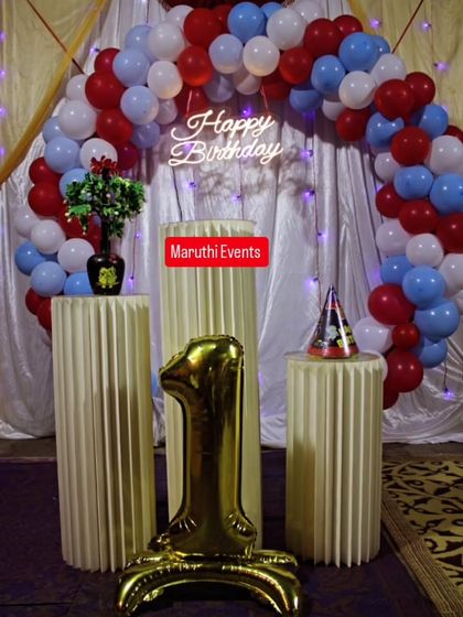 A simple and classic first birthday setup. The red, white, and blue balloon arch is paired with elegant white plinths and a large number "1" balloon.