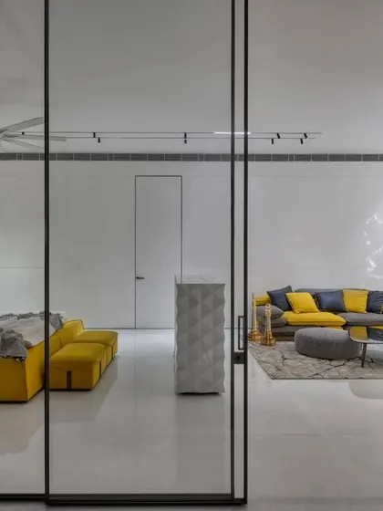 A bright and airy bedroom and living area from the 'Vrinda' project. The use of a yellow sofa and bed brings a pop of color to the otherwise minimalist white space, creating a cheerful and modern feel.