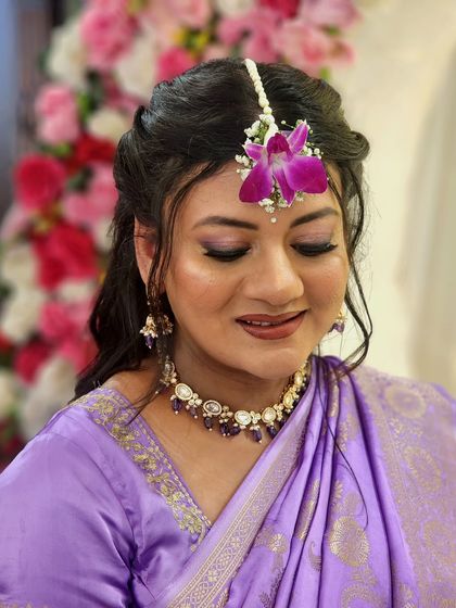 A glowing mommy-to-be in a lovely lilac saree for her baby shower, with her makeup featuring soft purple tones on the eyes.