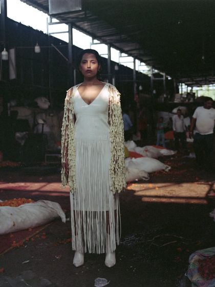 Another perspective of the jasmine flower jacket and fringe dress. This head-on shot highlights the contrast between the delicate floral piece and the stark, industrial feel of the market warehouse.