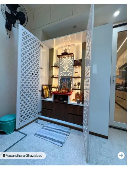 A spacious pooja room with geometric jaali doors and a backlit 'Om' symbol. The design provides ample space for rituals and storage, combining functionality with spiritual aesthetics.