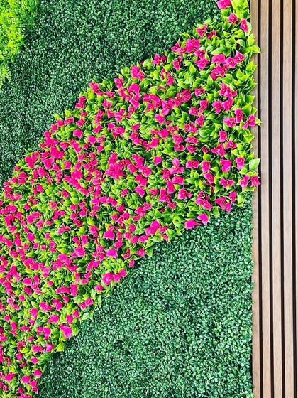 I can create patterns on green walls using different colored flowers and leaves. This wall panel features a sweeping design of pink flowers against a dense green backdrop, adding a dynamic and artistic touch. This is a great way to create a feature wall for an event or a permanent office installation.
