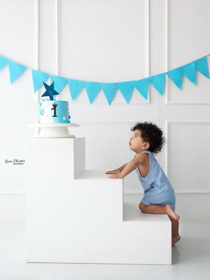 A candid shot of the birthday boy looking up towards his cake, ready for the fun to begin. The simple setup with a blue banner is perfect for this classic theme.