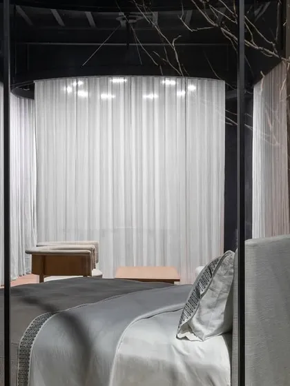 This view frames the bed display as a serene composition. Seen through the store's structural elements, the bed appears as a sanctuary, reinforcing the brand's ethos of quiet luxury and the home as a place of retreat.