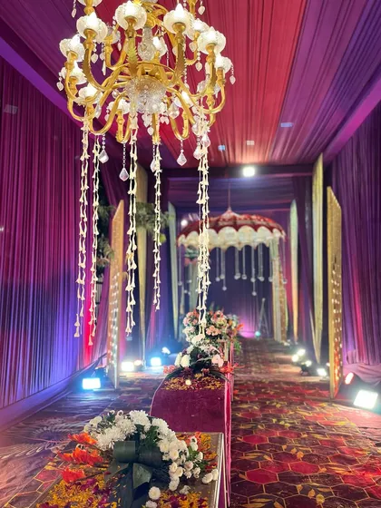 An entrance that glows with elegance, featuring purple fabric, hanging chandeliers with floral tassels, and beautifully arranged centerpieces.