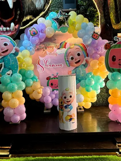 The full Cocomelon stage setup, showing the character cutouts, balloon arch, and themed pedestal.