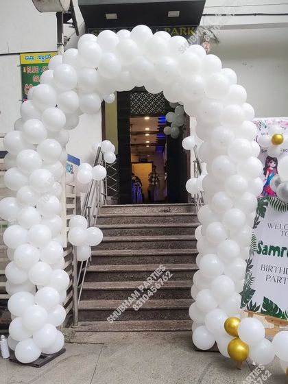 An elegant all-white balloon arch at the entrance of a building for a birthday party.