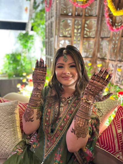 A happy bride showing both her hands, covered in our detailed and beautiful bridal mehandi.