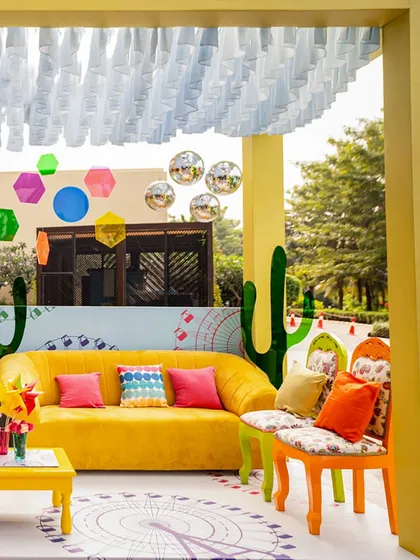 The full view of the Coachella-themed lounge cabana. The setup includes a bright yellow sofa, colorful chairs, a custom-printed floor, and hanging disco balls, creating the perfect festival chill-out spot.