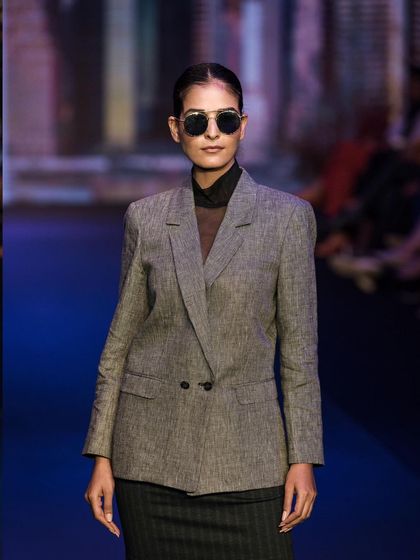 A powerful runway look featuring a grey double-breasted blazer and sunglasses. The shot captures the modern, professional aesthetic of the designer's collection.