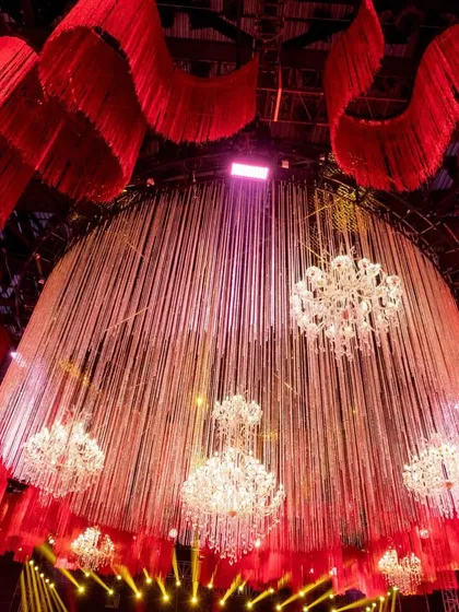 An upward view of the central ceiling installation, showing the interplay between the dense red fabric tassels and the delicate, cascading crystal threads, punctuated by the sparkle of chandeliers.