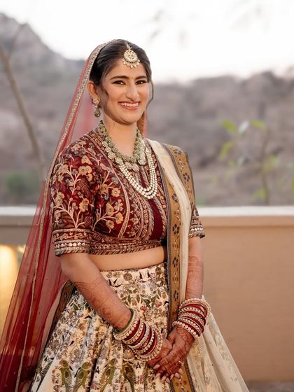 A portrait of bride Sneha in her custom JJ Valaya wedding lehenga. The combination of a deep red blouse with an ivory, delicately printed skirt offers a fresh take on the traditional bridal palette.
