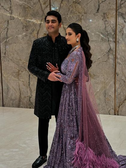 A full-length view of Sree and Mohnish's sangeet outfits. Her feathered purple lehenga and his classic black sherwani create a modern and stylish couple's look.