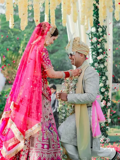 The groom gets down on one knee during the Varmala ceremony, a modern and romantic twist on a classic tradition, captured at a beautiful outdoor wedding.