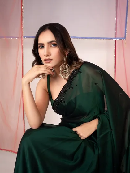 A seated portrait showcasing a deep green saree. The lighting is soft and flattering, creating an elegant and composed mood for the brand's catalog.