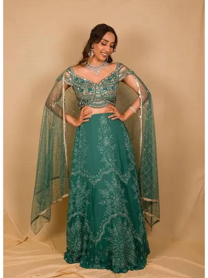 This elegant teal green lehenga features delicate silver embroidery and unique, flowing cape-style sleeves. It's a sophisticated and modern take on the traditional lehenga, perfect for a wedding guest.