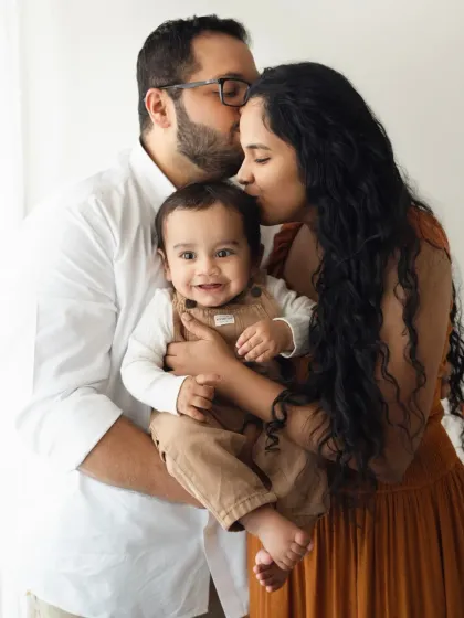 A beautiful family of three, with both parents kissing their smiling baby. This is a classic and loving family portrait.