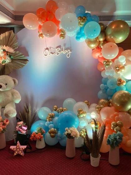 This vibrant baby shower setup features a fun color combination of blue, orange, and gold balloons. The design includes a large white teddy bear, an "Oh Baby" neon sign, and floral arrangements for a cheerful look.