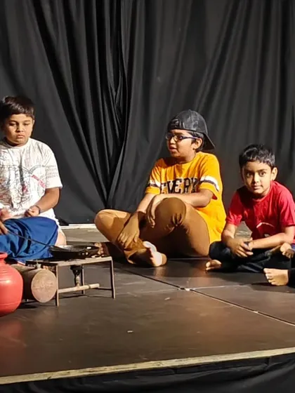 A heartwarming scene from a children's play, where kids are seated on stage listening to a story from an elder.
