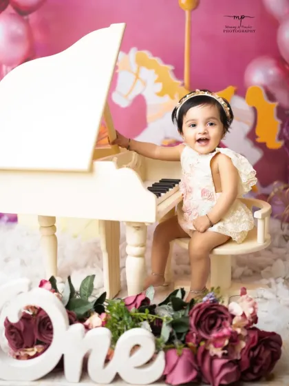 A little musician celebrates her first birthday at a miniature grand piano. This whimsical setup with pink balloons and florals is perfect for a sweet and artistic portrait.