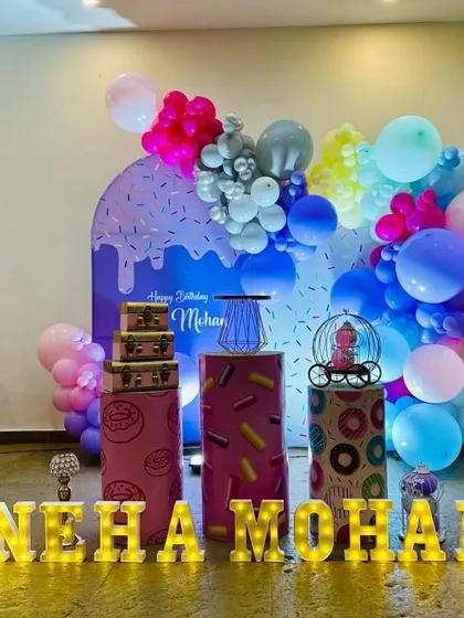 A delicious-looking donut and sweets theme for Neha and Mohan. This setup features donut-printed pedestals and a colorful balloon arch against a sprinkle-themed backdrop.