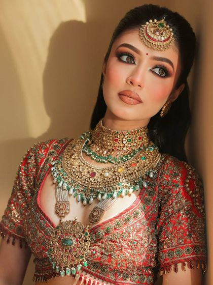 The very definition of a Royal Indian Bride. This look features bold, kohl-rimmed eyes and contoured cheeks, perfectly complementing the heavy, traditional jewelry and red lehenga.