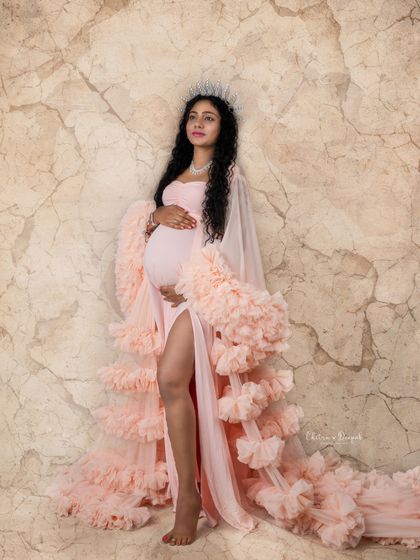A goddess pose against a marble-textured backdrop. This mom-to-be looks regal and powerful in a soft pink gown and silver crown.