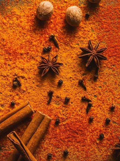 A close-up flat lay of spice powders and whole spices like star anise and cinnamon. The warm, intense lighting and dark background create a fiery and dramatic mood.
