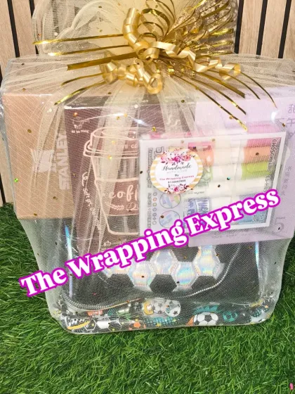 A return gift hamper for a kid's party, containing a football-themed pouch, a Stanley mug, and some stationery items, all wrapped in net.