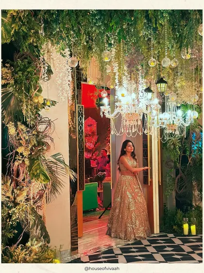 The bride poses at the entrance to the enchanted forest Sangeet, where a ceiling of cascading greenery, crystal chandeliers, and vintage lanterns creates a magical, fairytale-like setting.