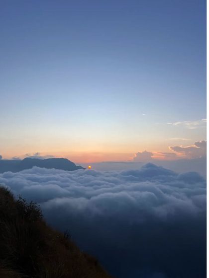 The sun peeking over the horizon above a sea of clouds, as seen from the Munnar trek.