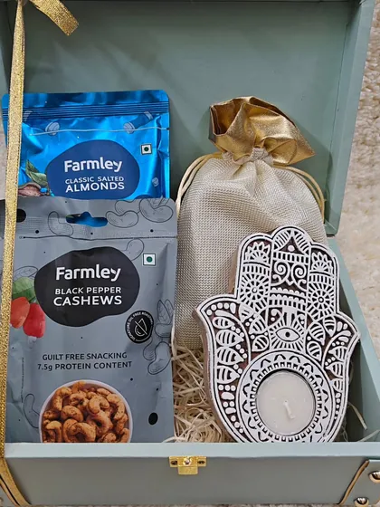 An open view of the exclusive trunk box, showing the curated selection of Farmley cashews, almonds, and a Hamsa tealight holder.