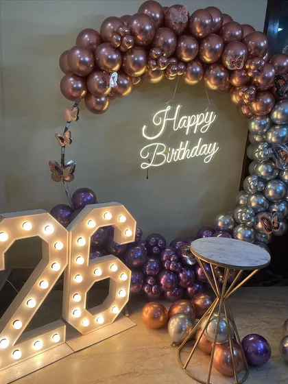 This is a duplicate of ID 37, 80, 136, 139, 151, 158, 203. A stylish half-arch balloon ring for a 26th birthday. This home decoration uses chrome rose gold and silver balloons, a neon sign, and marquee numbers.