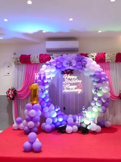 A beautiful purple and white balloon ring for a combined birthday and anniversary celebration. The setup includes a light-up number '1' and a custom neon sign.