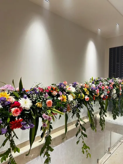 A lush floral runner along the staircase railing, filled with a variety of colorful blooms and cascading greens, added a touch of elegance to the housewarming decor.