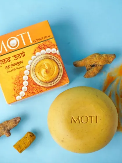 A clean, top-down product shot of a luxury soap bar next to its packaging and raw turmeric ingredients. This style of e-commerce photography emphasizes product details and natural components for online stores and advertisements.