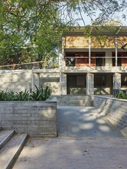 The CEPT University Canteen is nestled between mature trees, with its structure carefully integrated into the existing landscape. The use of concrete steps and planters helps to merge the building with its site.