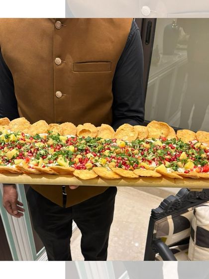 Our Papdi Chaat board is the life of the party. A server presents a long wooden board layered with crispy papdi, yogurt, chutneys, and fresh garnishes, ready to be shared.