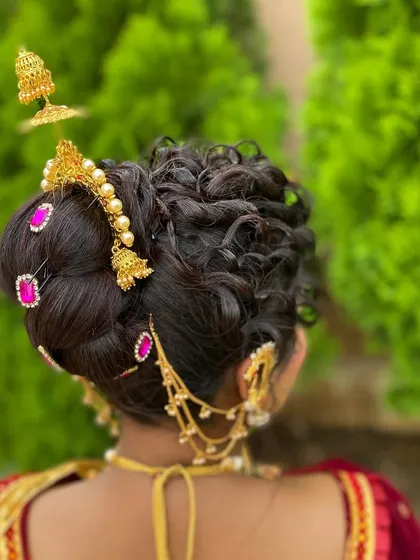 The back view of a traditional bridal updo. This style showcases intricate curls and the placement of classic temple jewelry, including jhumkas and hairpins, for a complete ceremonial look.
