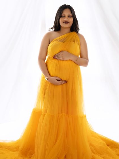 A serene portrait of a mom-to-be in a yellow gown, eyes closed, peacefully cradling her baby bump.