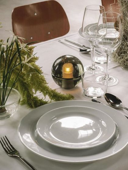 The Bocci 14p in smoked grey sits on an elegantly set dining table, serving as a modern, reusable alternative to candles.