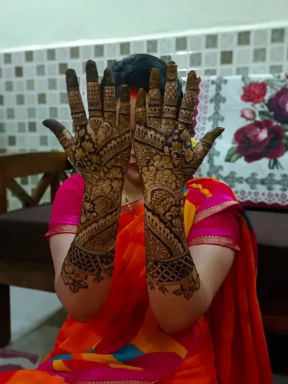 A happy client showing off her elaborate mehndi. The design covers both hands and forearms with traditional motifs, perfect for a big celebration.