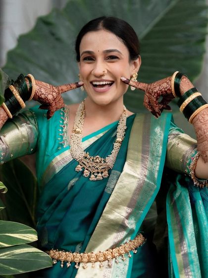 Another joyful, candid moment that shows off the bride's complete look, from her happy expression to the elegant fall of her saree and the intricate gold jewelry.