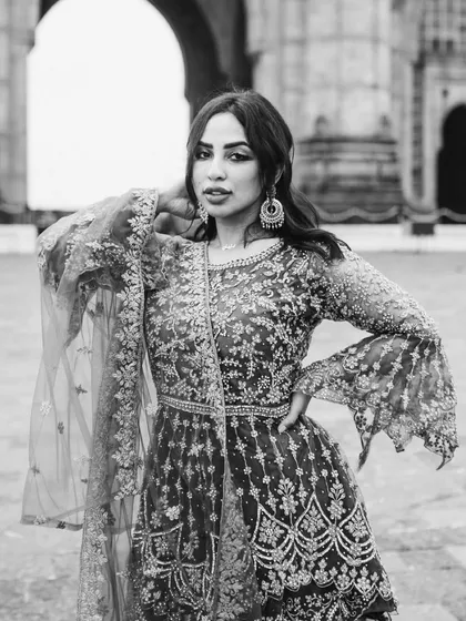 A glamorous black and white portrait of a bride. The monochrome treatment emphasizes the intricate details of her embroidered gown and her confident pose.