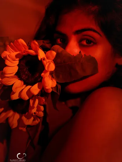 A bold and intimate portrait using a sunflower as a prop. The intense red light creates a fiery and passionate mood.