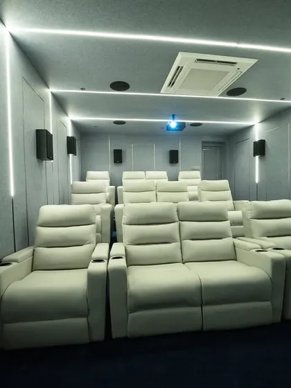 A stunning example of a modern home cinema in Madurai, featuring clean lines and a cool color palette. The bright white recliners contrast beautifully with the grey acoustic-paneled walls and blue carpet, while integrated LED strips provide a futuristic ambiance.