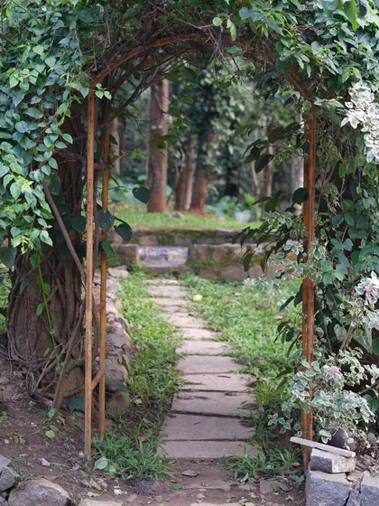 A simple, rustic archway covered in vines creates a magical entrance to a stone pathway, inviting you to explore the garden beyond.