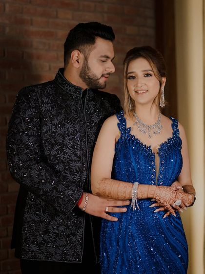 An intimate portrait of the couple during their engagement event. The groom embraces the bride from behind as she smiles, showcasing their beautiful blue and black coordinated outfits.