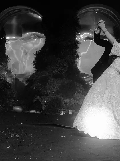 A classic dance pose captured in dramatic black and white. This timeless shot emphasizes the couple's grace and the flowing movement of the bride's gown against a dark, moody backdrop.